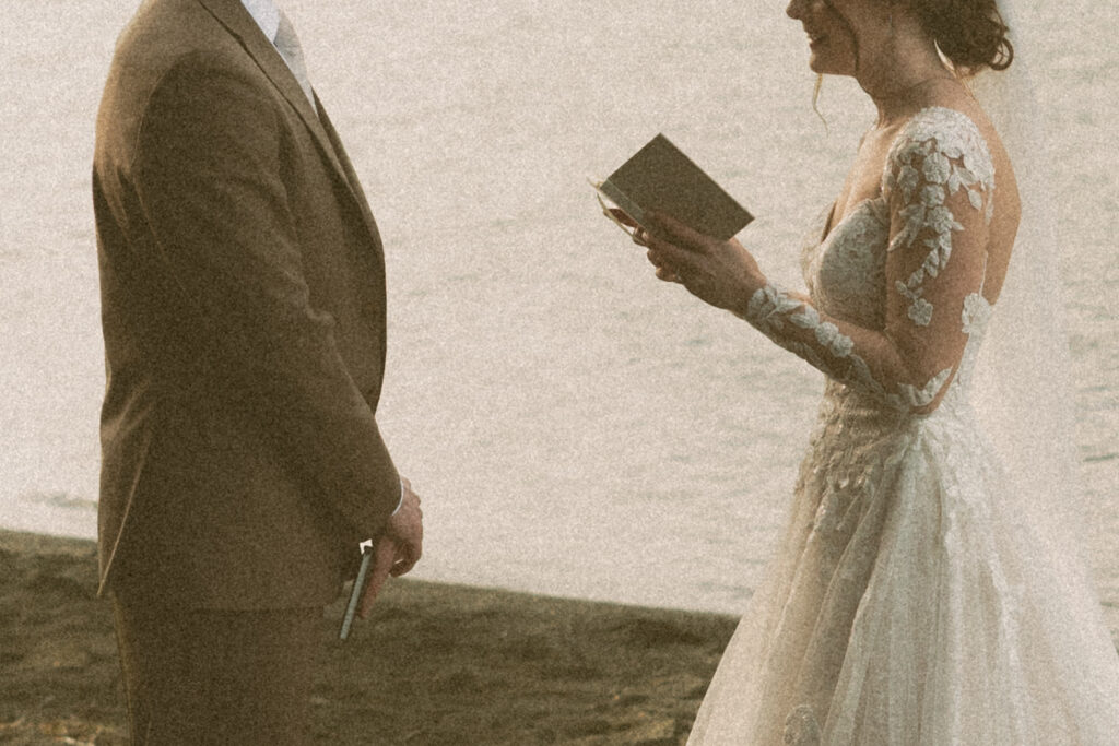 A grainy, cinematic photo of a bride reading her handwritten vows to her husband next to the water at their Lake Crescent Wedding
