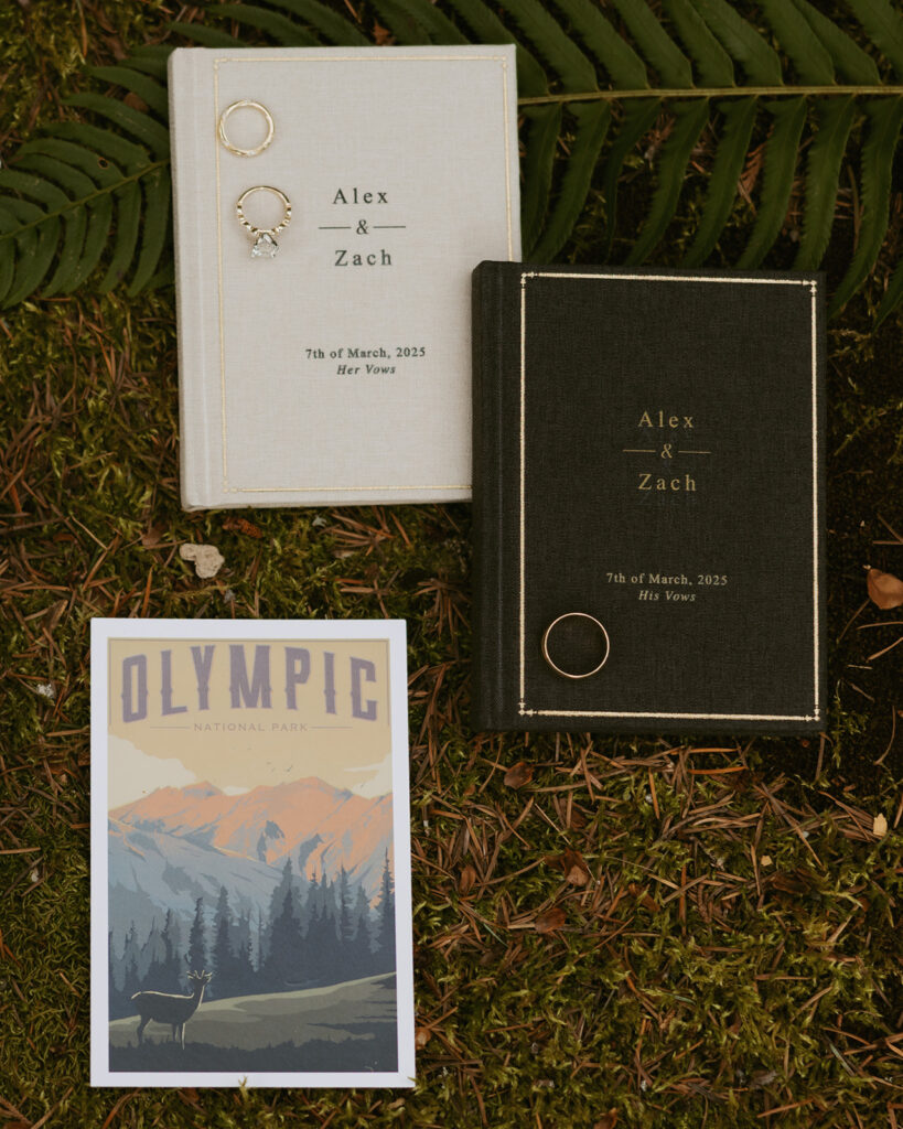 A flat lay of wedding rings setting atop green & white embossed vow notebooks are displayed at an olympic national park wedding