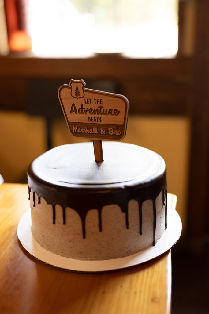 A wedding cake is photographed with a wooden cake topper reading 'Let the adventure begin' following a Washington elopement at Artist Point