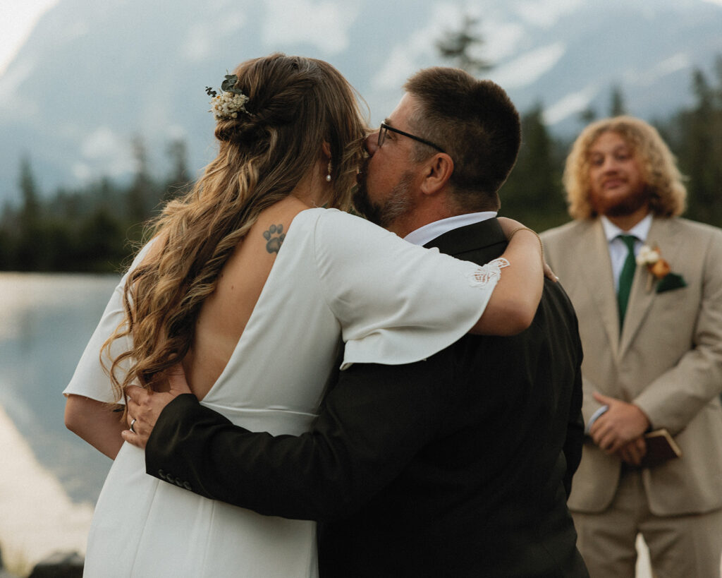A bride receives a kiss on the cheek from her father has he gives her away at her Washington elopement