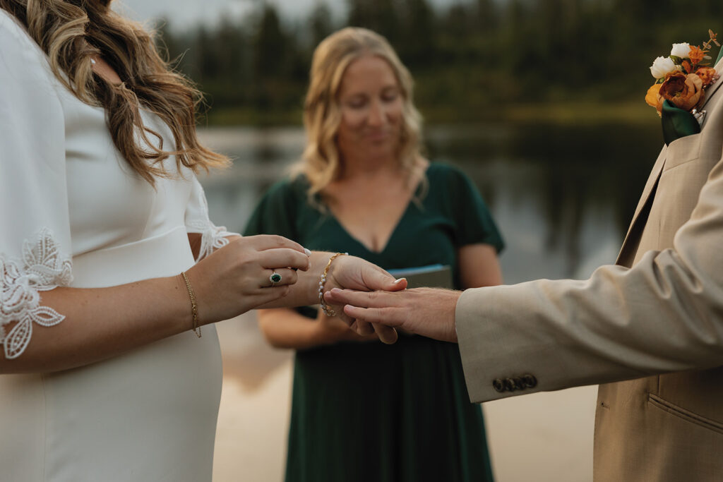 A bride slips a wedding band on her groom's finger as they elope in Washington at Mt. Baker
