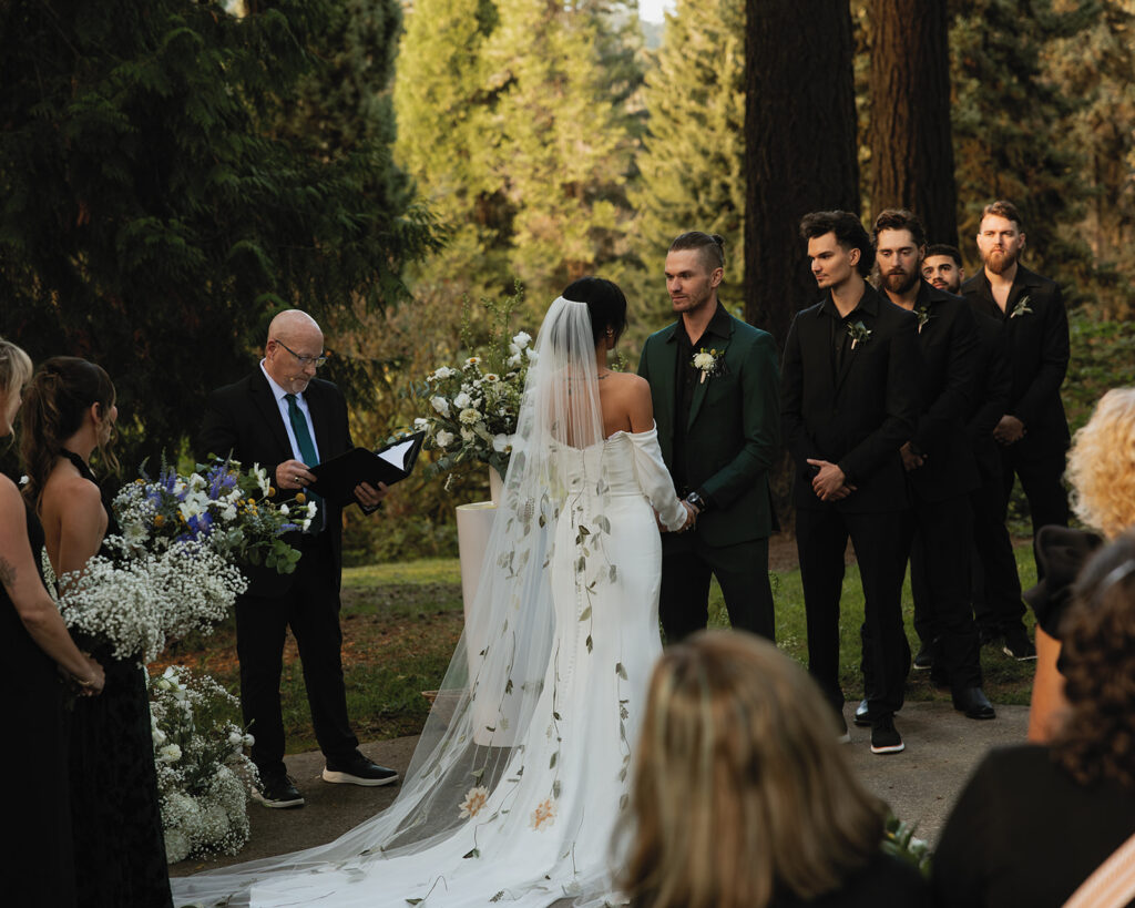 A bride wearing a veil with colorful floral details faces her groom at their hoyt arboretum portland wedding
