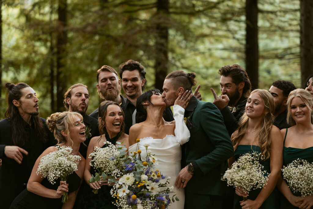 A wedding party smiles and cheers as the bride and groom share a kiss following their Hoyt Arboretum wedding in Portland OR