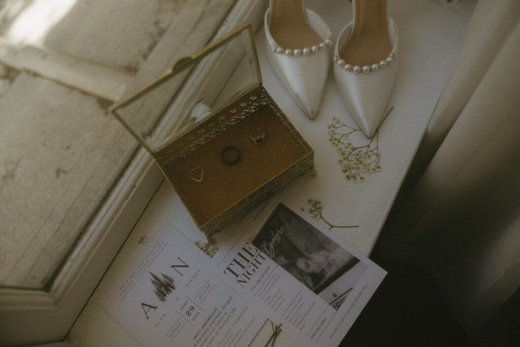 A detail photo shows white bridal shoes, wedding rings, and wedding invitations next to a window at The Sentinel in Portland 