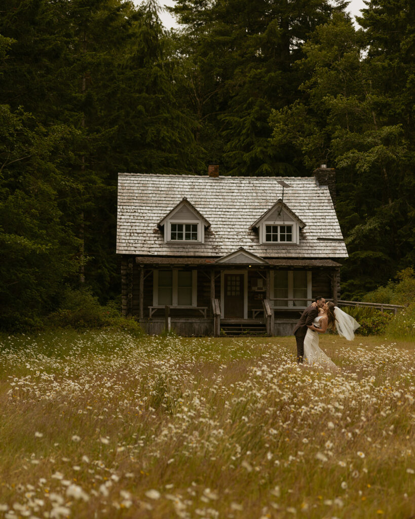 Newlyweds share a kiss in a field before a cabin during their Olympic National Park wedding