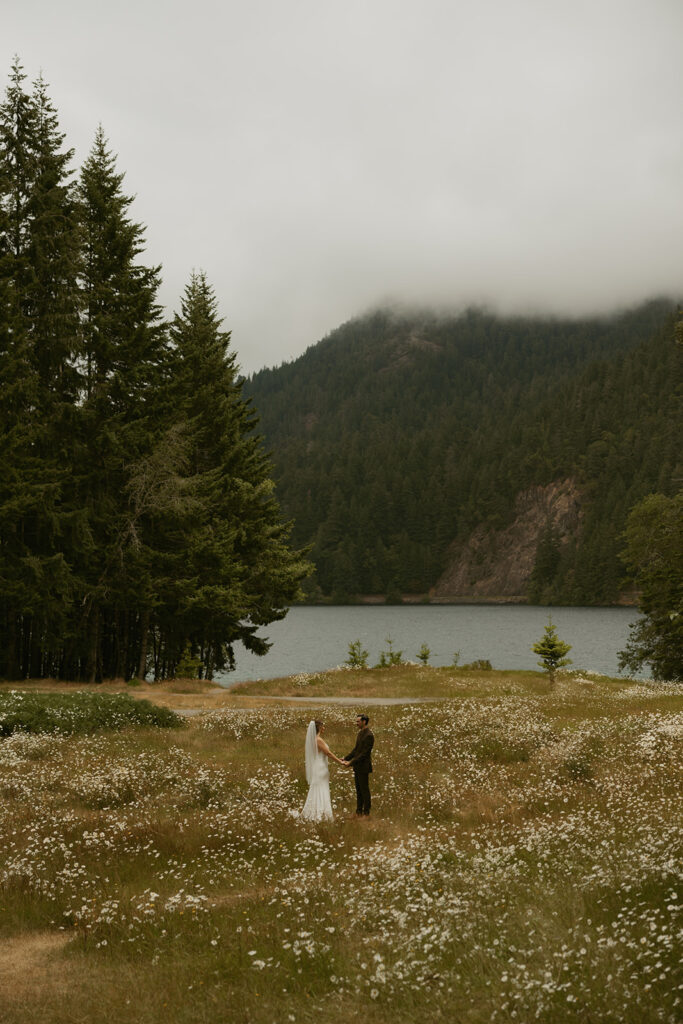 A bride and groom hold hands in a meadow near Lake Crescent on their Olympic National Park wedding day