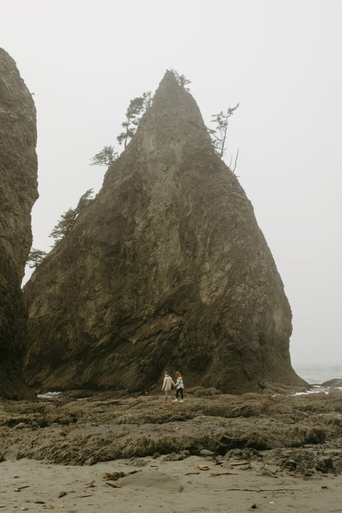 A couple is photographed in the distance beneath a rock formation at Rialto Beach, one of the things to do near olympic national park
