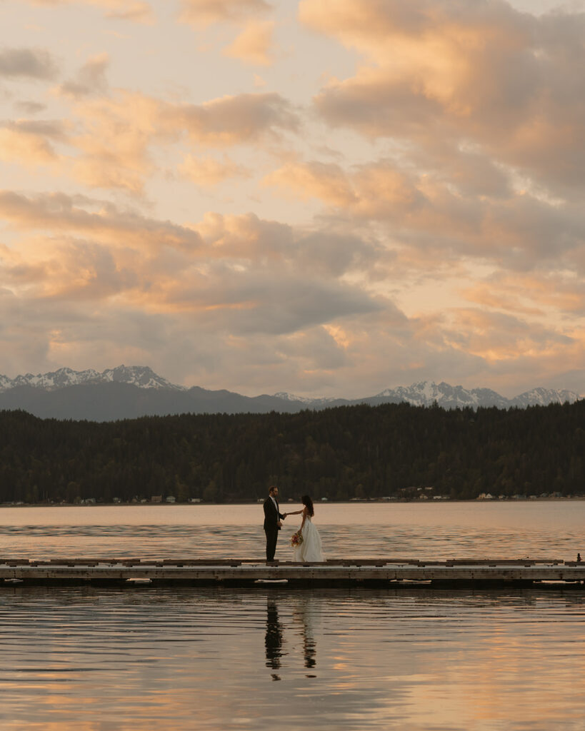 A couple is photographed in their wedding attire on a dock at sunset following their Washington elopement.