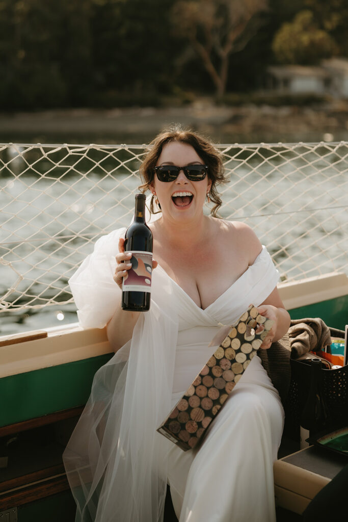 A bride poses in her wedding gown while holding a bottle of wine at Friday Harbor
