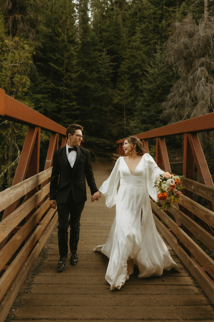 Newlyweds hold hands as they walk across a bridge following their Washington elopement ceremony.
