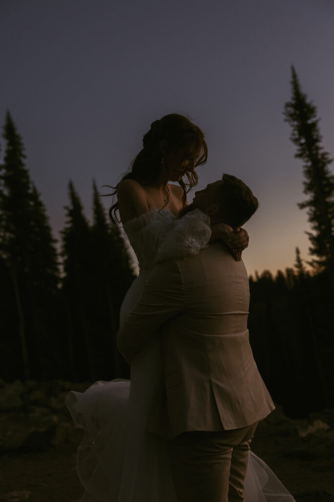 A newly married man lifts his bride in a photo at blue hour after eloping in Washington at Tipsoo Lake
