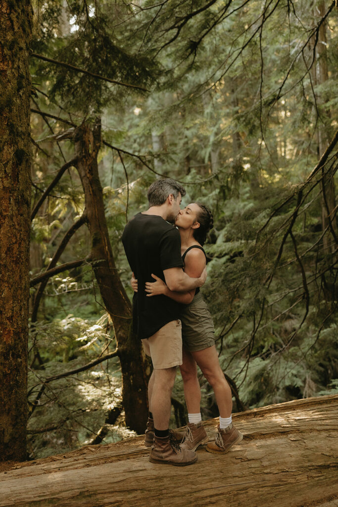 A couple shares a kiss as they balance on a fallen tree during their WA engagement photos 