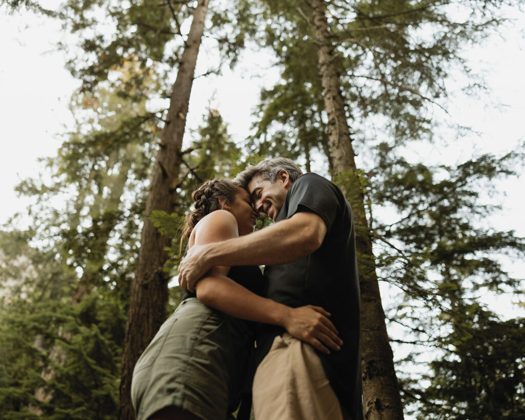 Seattle engagement photographers show a couple resting their foreheads against each other in the forest during an adventure engagement photo session 