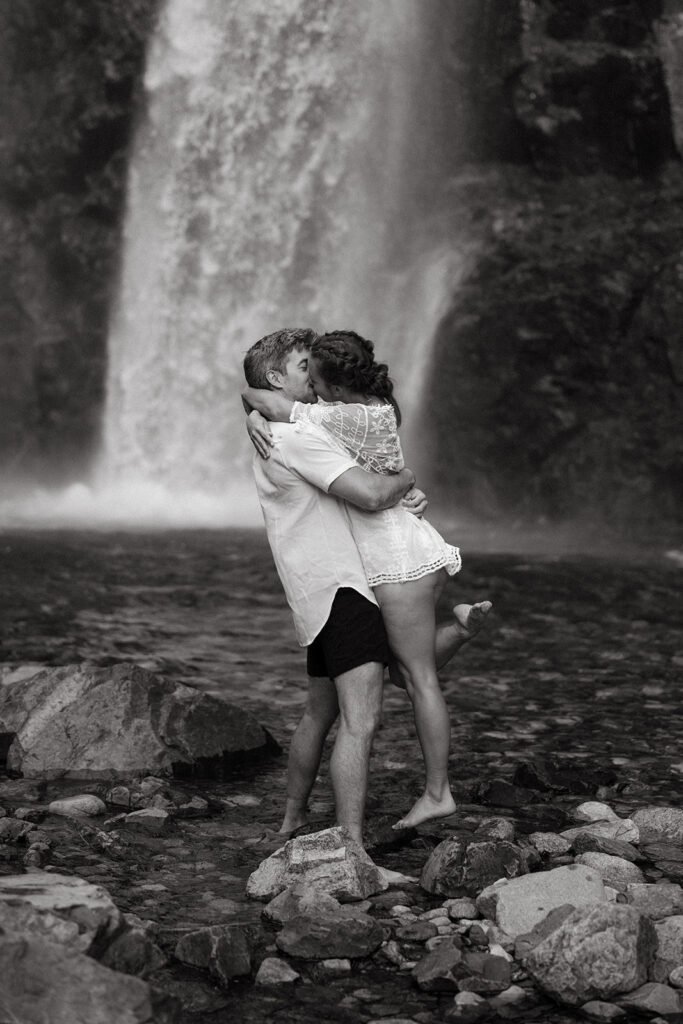 A man lifts his future bride for a kiss at Franklin Falls WA in a black and white image by Washington engagement photographer, Tessa Marie Collective 