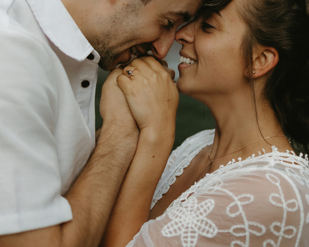 A photo of a couple wearing white highlights a woman's engagement ring as her fiancé kisses her hand in a photo by Seattle engagement photographers