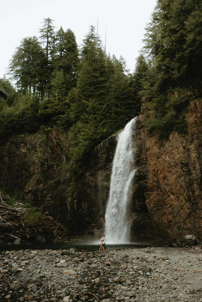A couple is pictured embracing from a distance at the base of Franklin Falls WA 