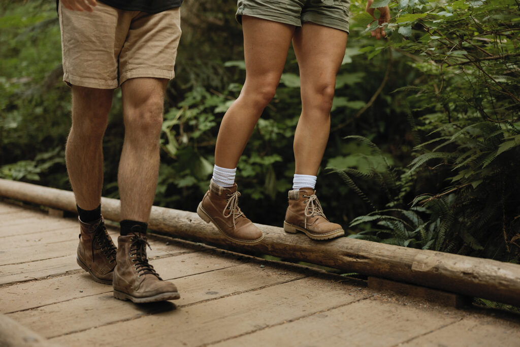 A close-up image shows a couple's hiking boots as they hike across a wooden bridge in engagement photography Seattle WA