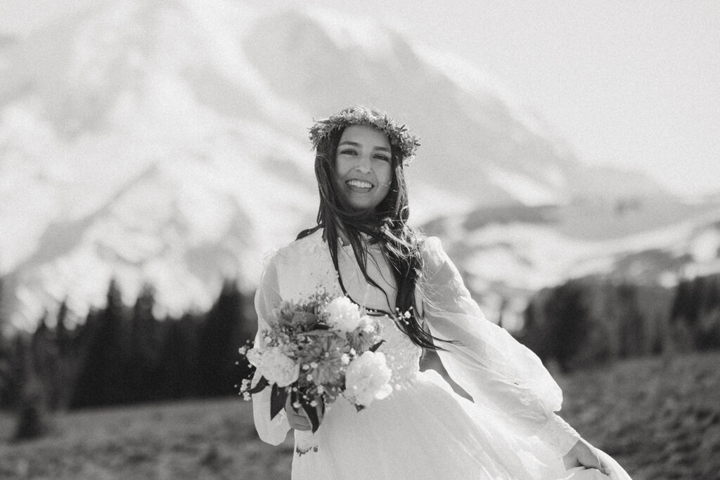 A black and white image depicts a young woman with long, dark hair holding a bouquet in her wedding dress at her mount rainier national park elopement
