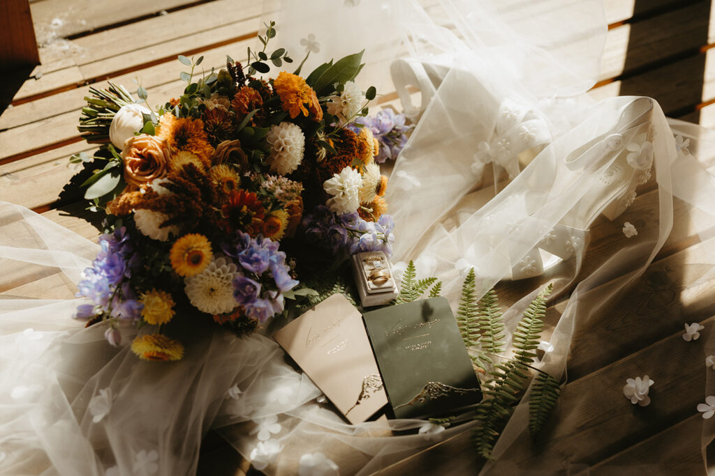 A bridal bouquet is photographed atop a veil with rings & vow books at a mount rainier elopement
