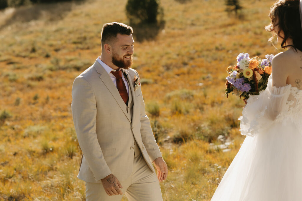 A mount rainier elopement first look is captured showing a smiling groom and a bride wearing an off-the-shoulder gown