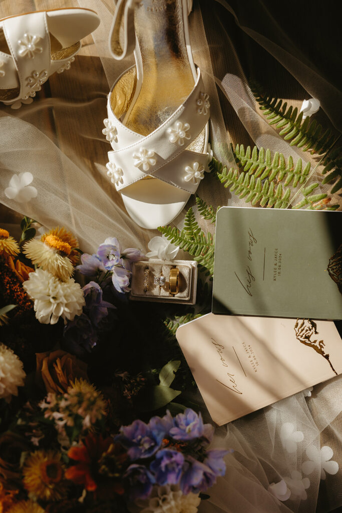 Colorful florals, vow books, rings, & white shoes are shown in a flat lay from a Mount Rainier wedding detail shot