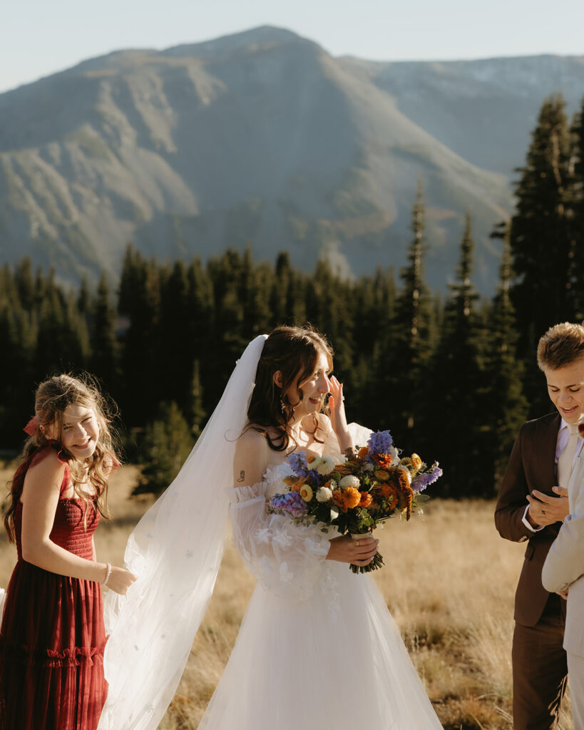A bride dabs a tear away as she holds her bouquet at her Mount Rainier wedding ceremony
