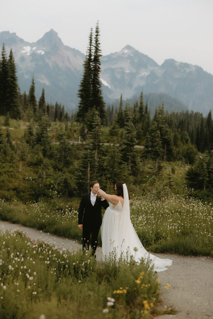 A couple is photographed at their Mt Rainier elopement in their wedding attire surrounded by alpines & wildflowers