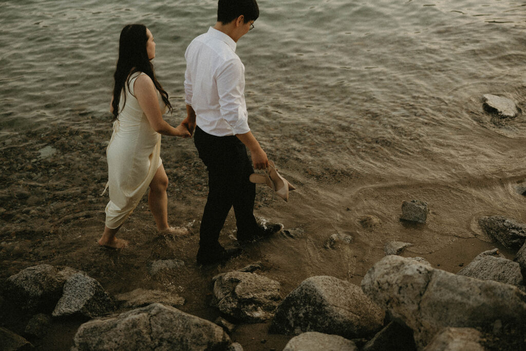 A couple holds hands as they walk along the water at Lake Chelan in a photo taken by engagement photographer washington state
