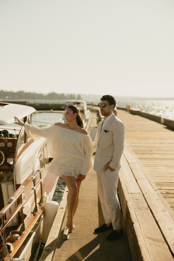 Newly engaged couple wearing a white dress and tan suit standing next to a boat on a dock