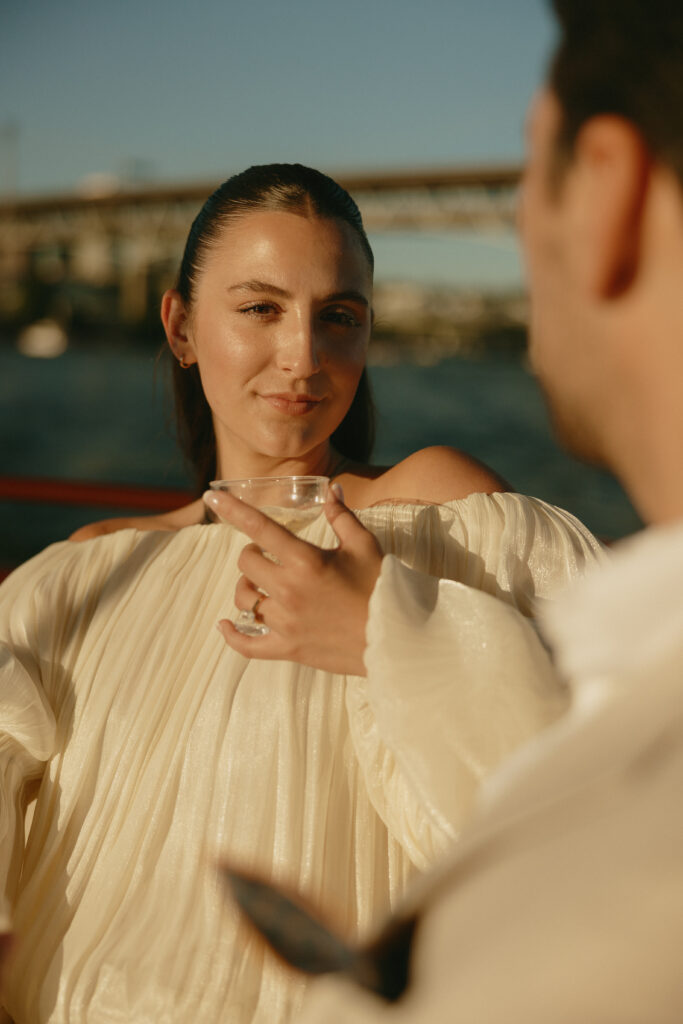A newly engaged couple looking at each other while drinking champagne on a boat