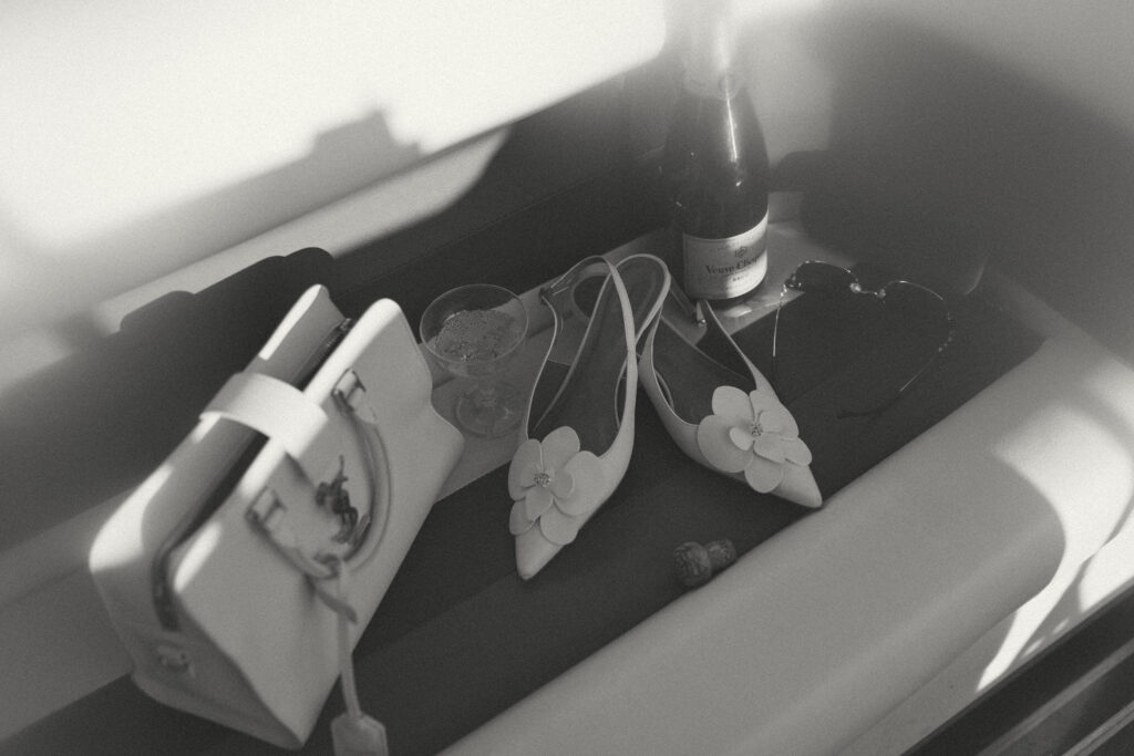 A white purse, white heels and champagne sitting together